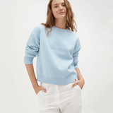 Woman wearing a light blue sweater with three additional sweaters displayed below on a white background.