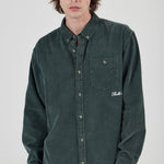 Person wearing a green button-up shirt with a brand logo on a white background