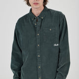 Person wearing a green button-up shirt with a brand logo on a white background