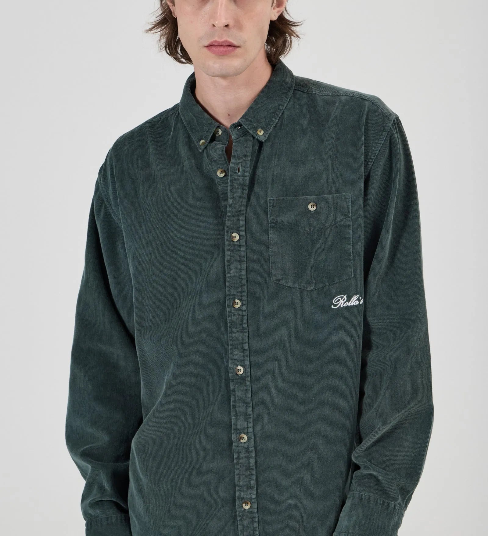 Person wearing a green button-up shirt with a brand logo on a white background