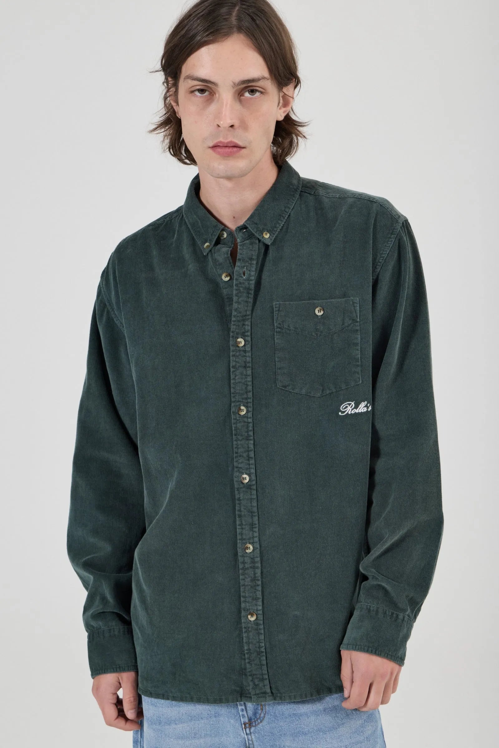 Person wearing a green button-up shirt with a brand logo on a white background