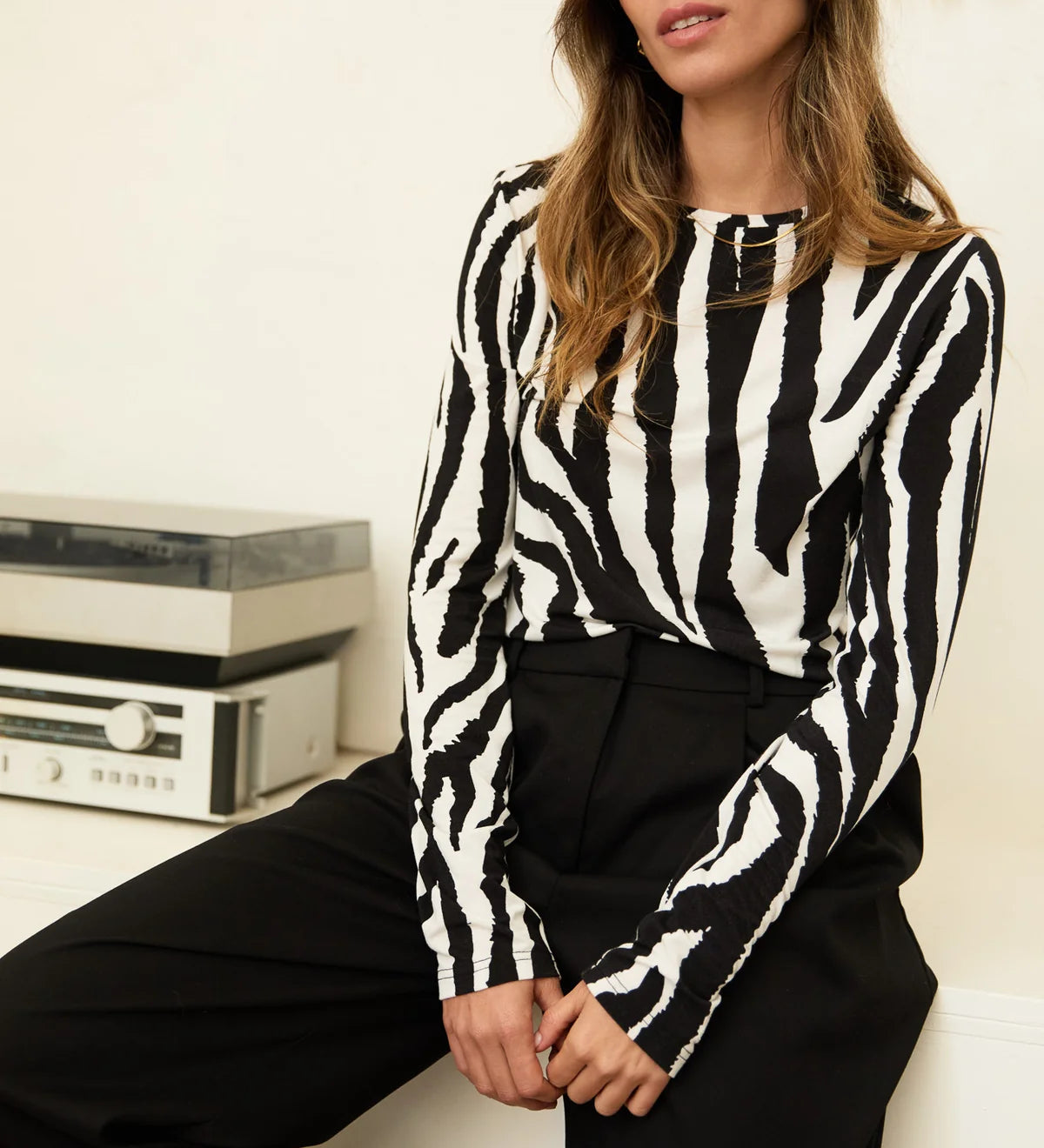Woman wearing a black and white zebra print top sitting on a white couch.