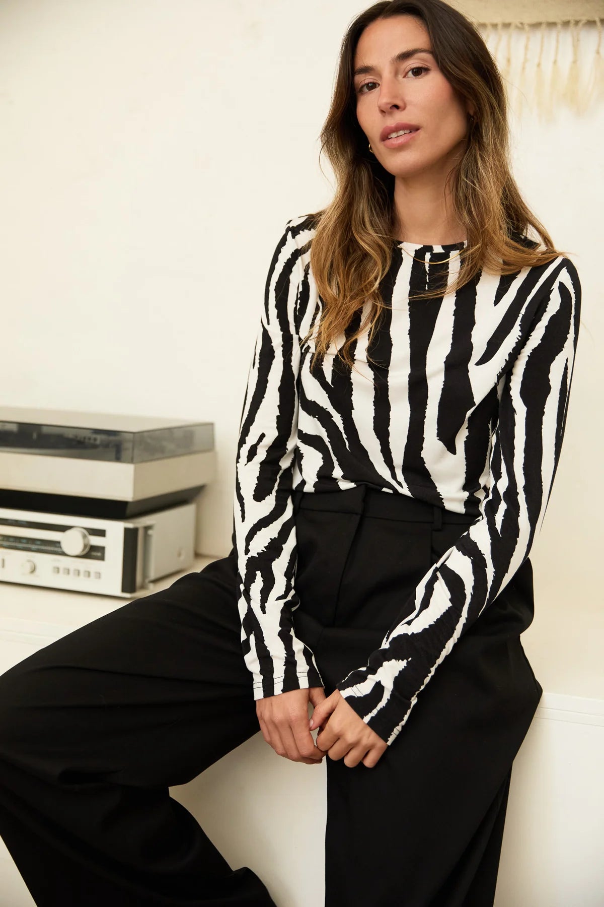 Woman wearing a black and white zebra print top sitting on a white couch.
