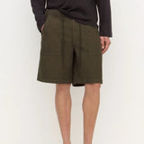 A model wearing olive green drawstring cargo shorts with side pockets, paired with a dark long-sleeve shirt and black clogs, standing against a plain white studio background.