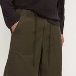 A person wearing olive green drawstring shorts with large front patch pockets and a dark long-sleeve top, photographed against a plain light background.