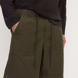 A person wearing olive green drawstring shorts with large front patch pockets and a dark long-sleeve top, photographed against a plain light background.