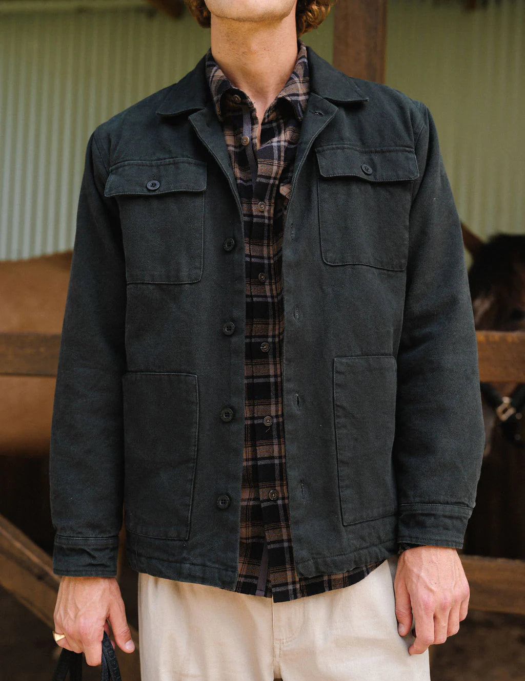 Person wearing a dark jacket over a plaid shirt with a blurred indoor background