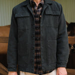 Person wearing a dark jacket over a plaid shirt with a blurred indoor background