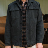 Person wearing a dark jacket over a plaid shirt with a blurred indoor background
