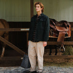 Man standing in a stable with horses and saddles in the background