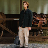 Man standing in a stable with horses and saddles in the background