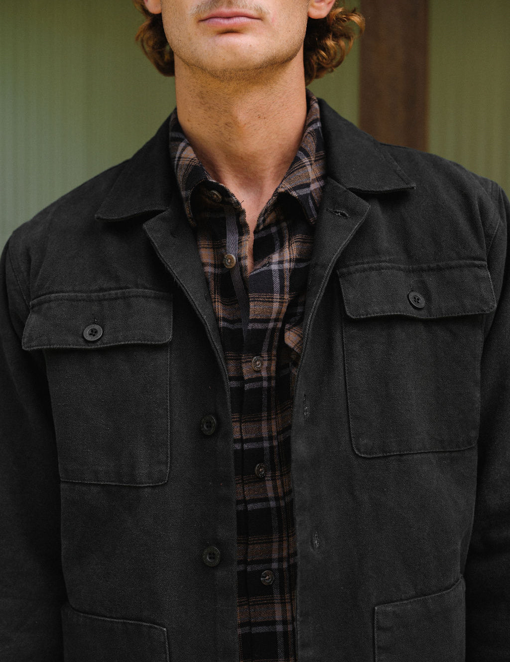 Man wearing a dark jacket over a plaid shirt with a neutral background