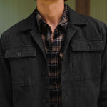 Man wearing a dark jacket over a plaid shirt with a neutral background