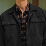 Man wearing a dark jacket over a plaid shirt with a neutral background