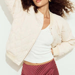 Woman wearing a white jacket, white top, and red striped skirt on a light background