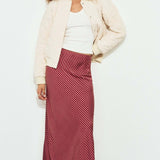Woman wearing a white jacket, white top, and red striped skirt against a white background