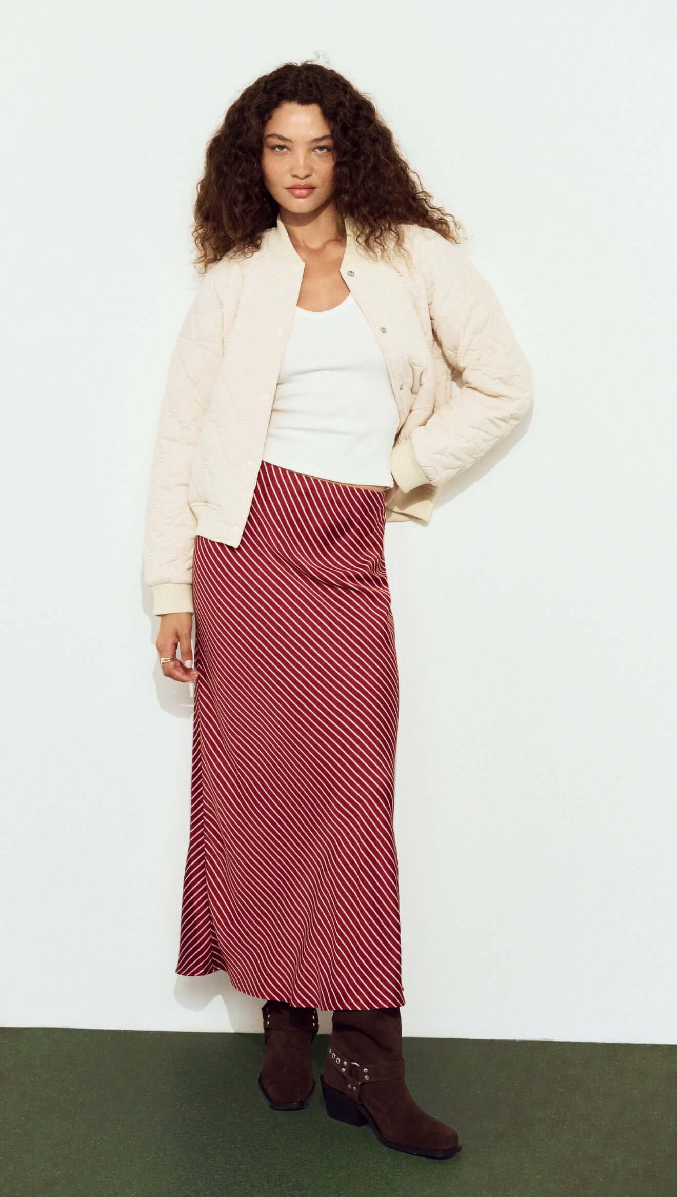 Woman wearing a white jacket, white top, and red striped skirt against a white background