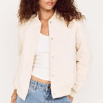 Woman wearing a cream blazer over a white top and blue jeans on a plain background