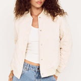 Woman wearing a cream blazer over a white top and blue jeans on a plain background