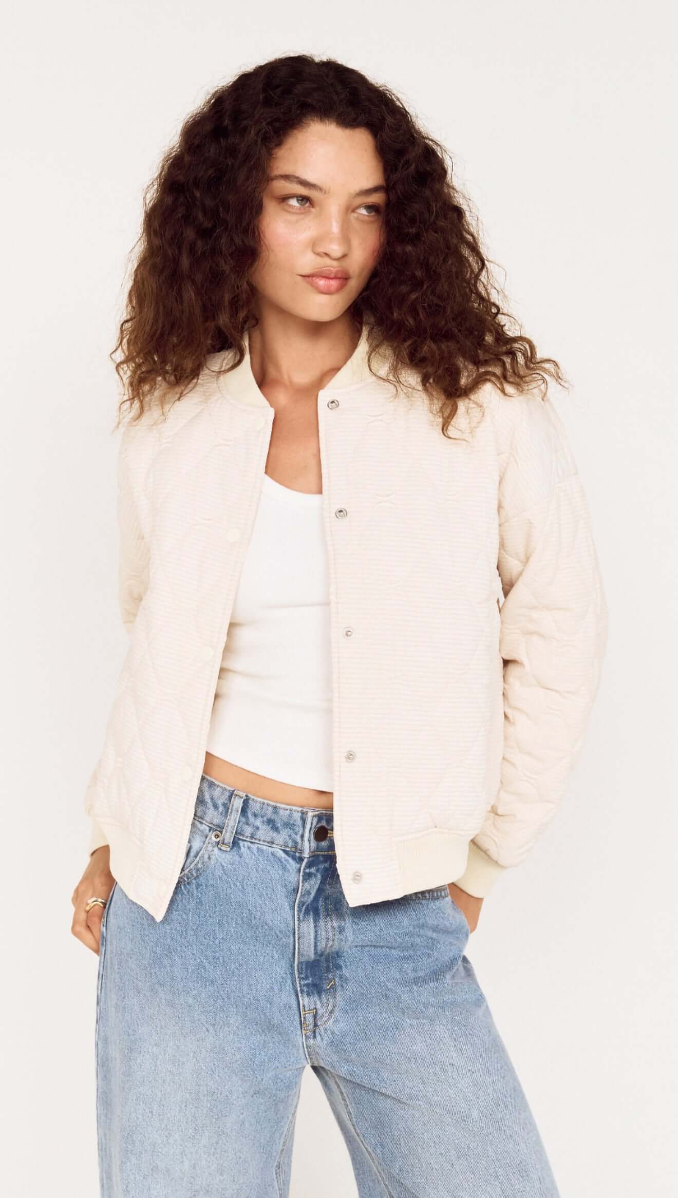 Woman wearing a cream blazer over a white top and blue jeans on a plain background