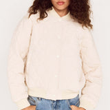 Person wearing a cream jacket and light blue jeans against a white background