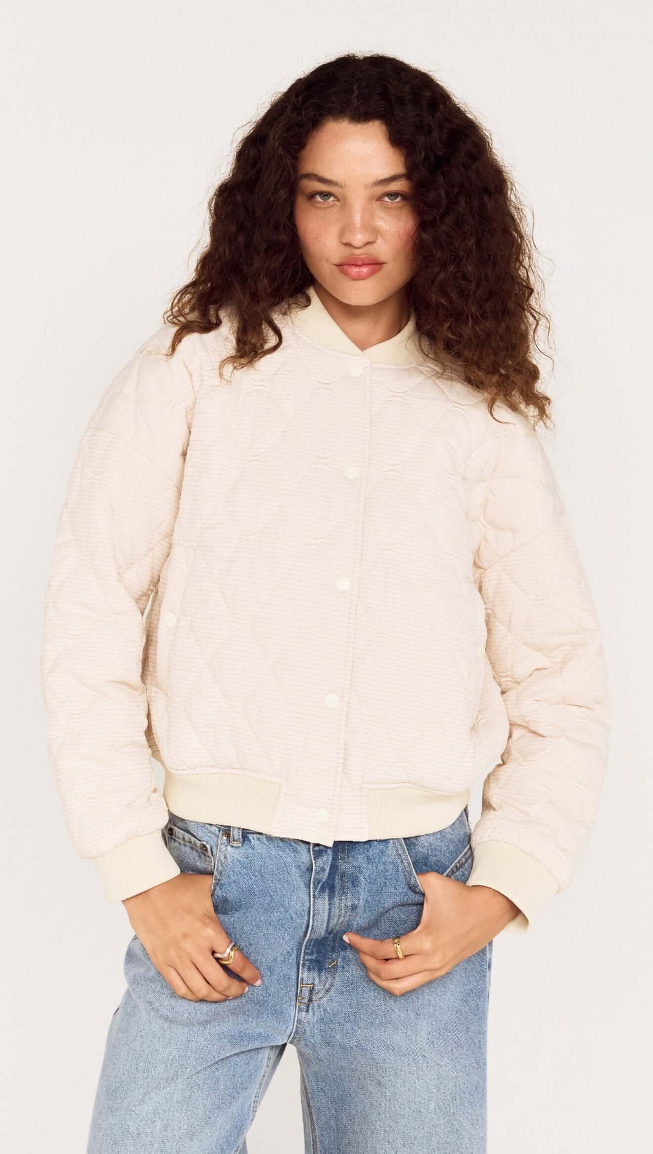 Person wearing a cream jacket and light blue jeans against a white background