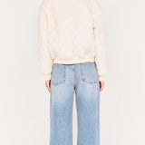 Person wearing a cream jacket and light blue jeans on a white background