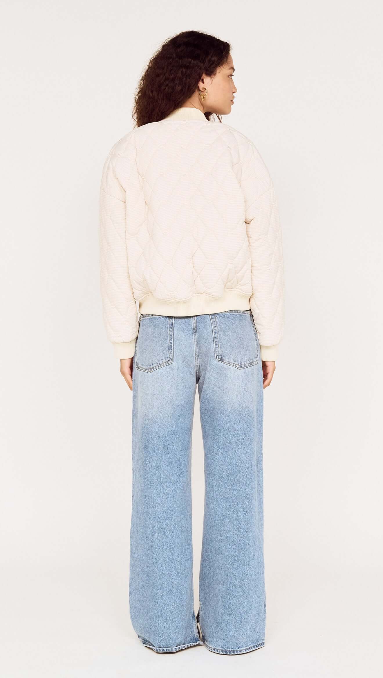Person wearing a cream jacket and light blue jeans on a white background