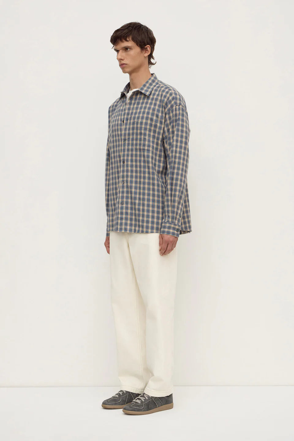 Man wearing a plaid shirt and white pants on a white background