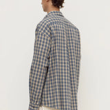 A man shown from the back wearing a blue and beige plaid button-up shirt and cream trousers, photographed against a plain white studio background.