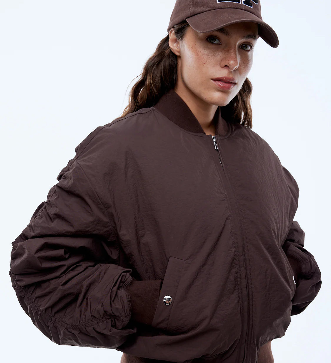 Woman wearing a brown jacket and cap with 'EP' logo on a white background