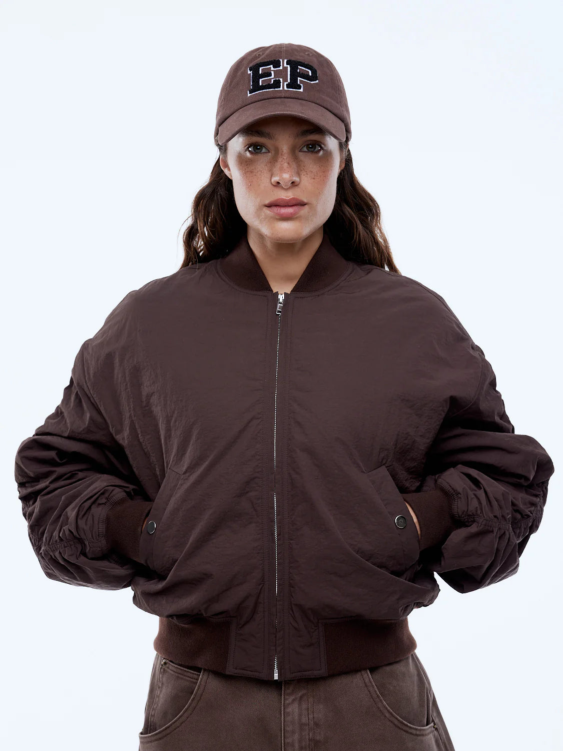 Person wearing a brown jacket and cap with 'EP' logo on a white background