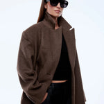 Person wearing a brown coat and sunglasses on a white background