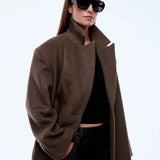 Person wearing a brown coat and sunglasses on a white background