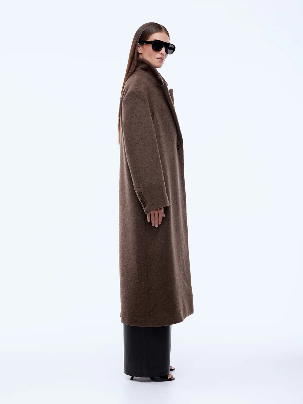 Woman wearing a long brown coat and sunglasses on a white background