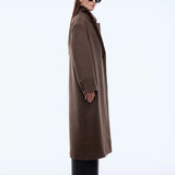Woman wearing a long brown coat and sunglasses on a white background