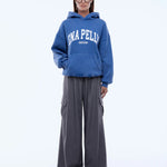 Person wearing a blue hoodie with 'ENAPELLY' branding and gray pants on a white background