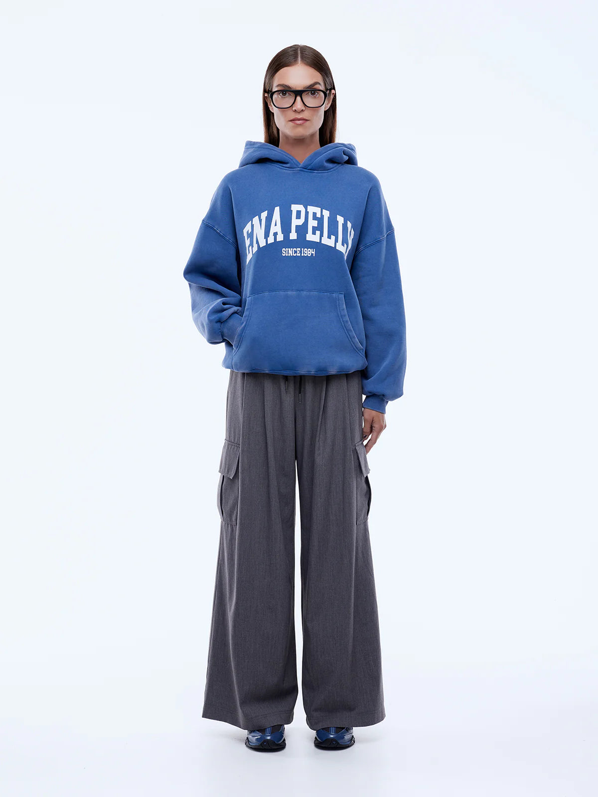 Person wearing a blue hoodie with 'ENAPELLY' branding and gray pants on a white background