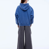 Person wearing a blue hoodie and gray pants on a white background