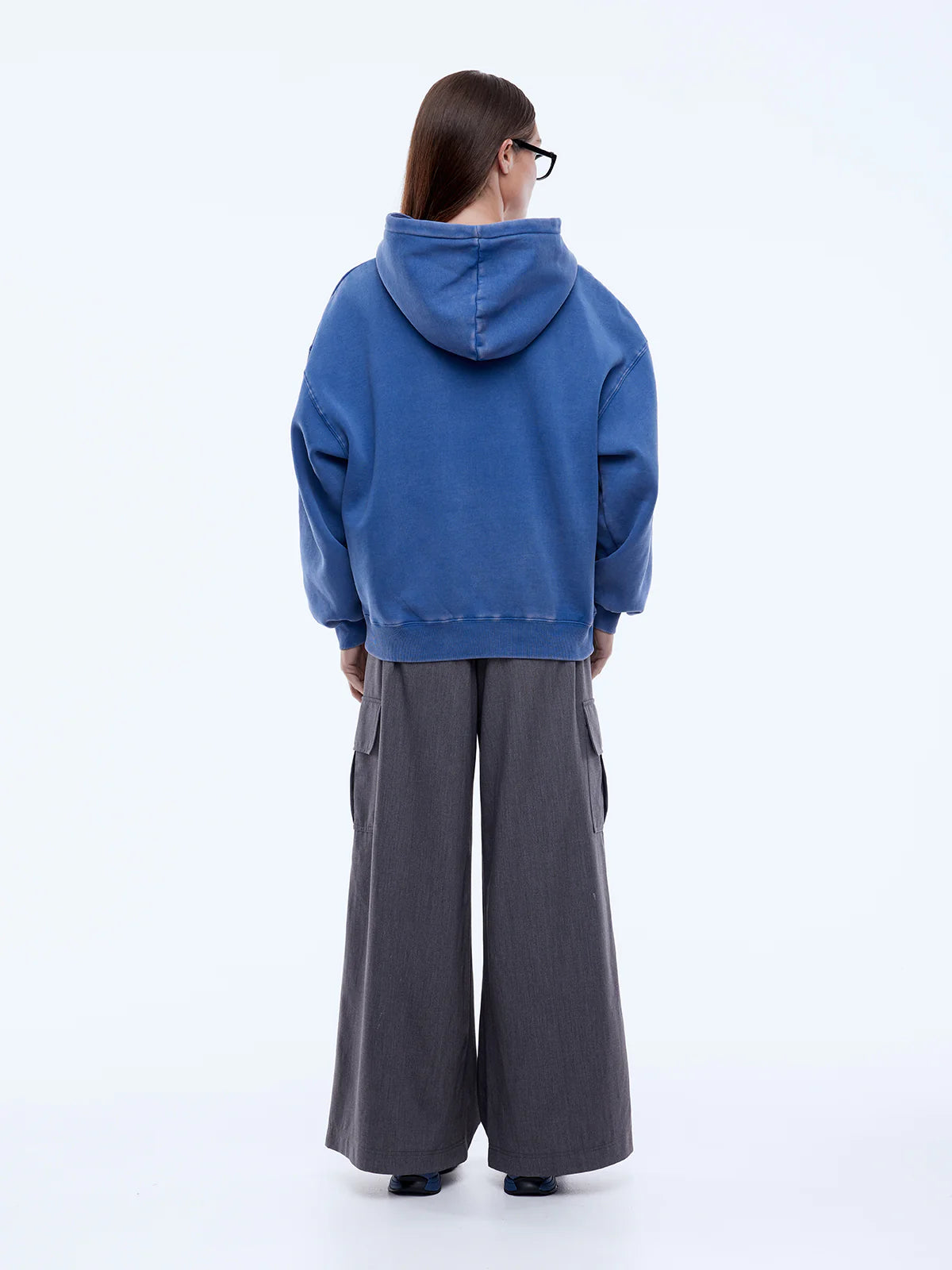 Person wearing a blue hoodie and gray pants on a white background