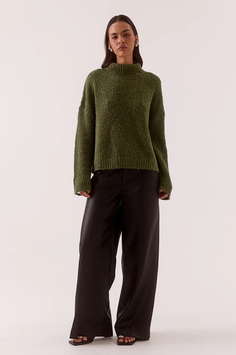 Woman wearing a green sweater and black pants on a white background