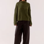 Woman wearing a green sweater and black pants on a white background