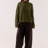 Woman wearing a green sweater and black pants on a white background