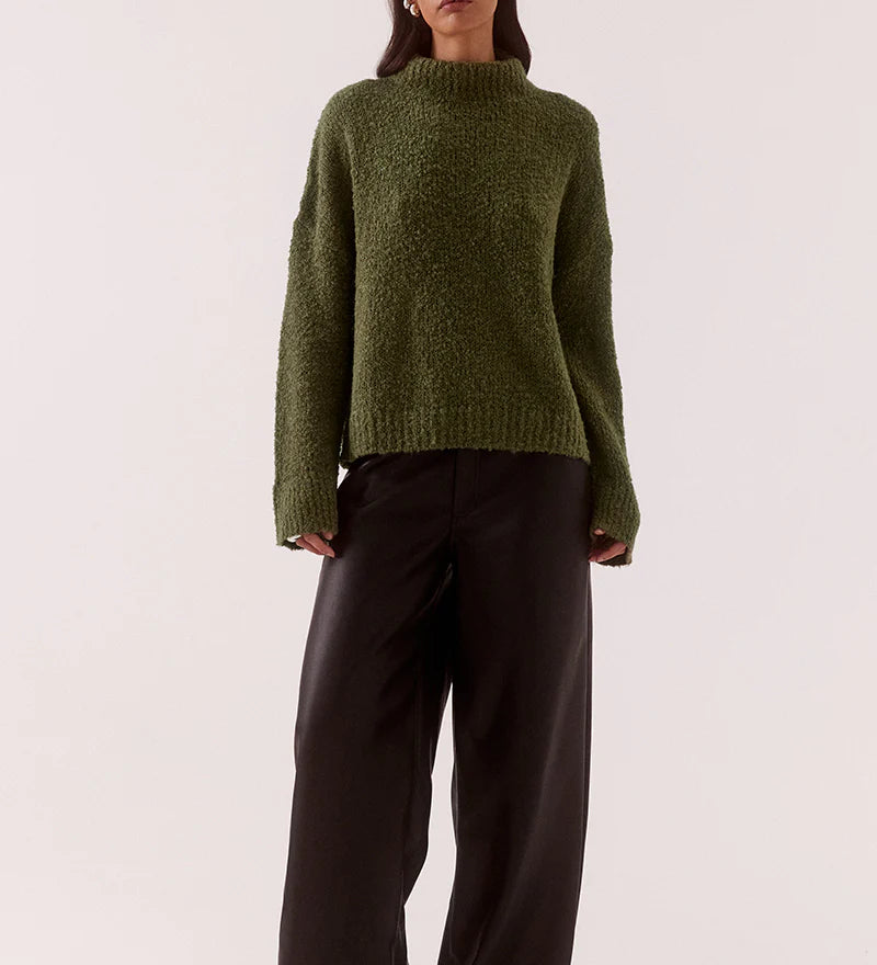Woman wearing a green sweater and black pants on a white background