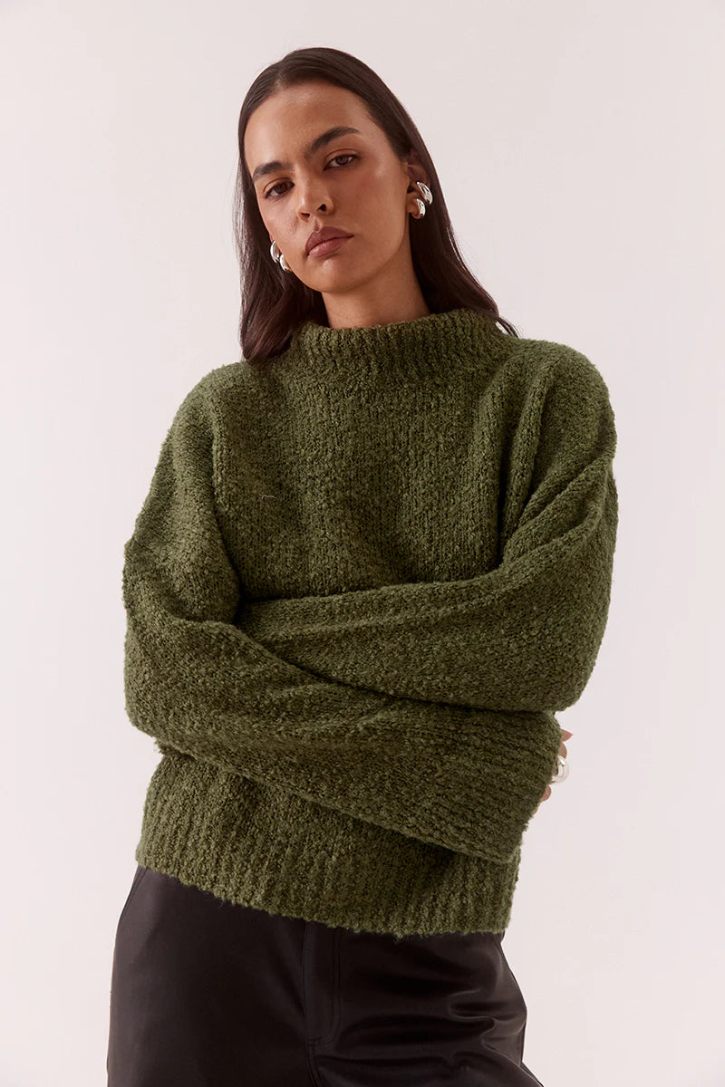 Woman wearing a green sweater and black pants on a white background