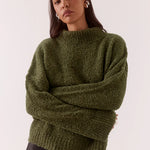 Woman wearing a green sweater and black pants on a white background