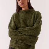 Woman wearing a green sweater and black pants on a white background