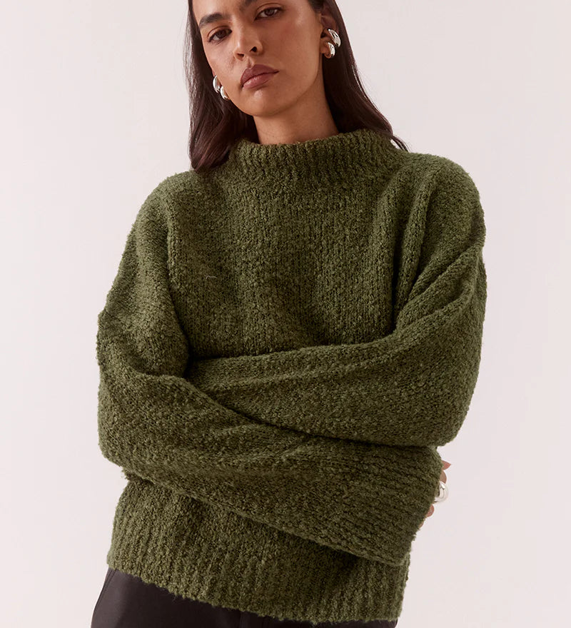 Woman wearing a green sweater and black pants on a white background