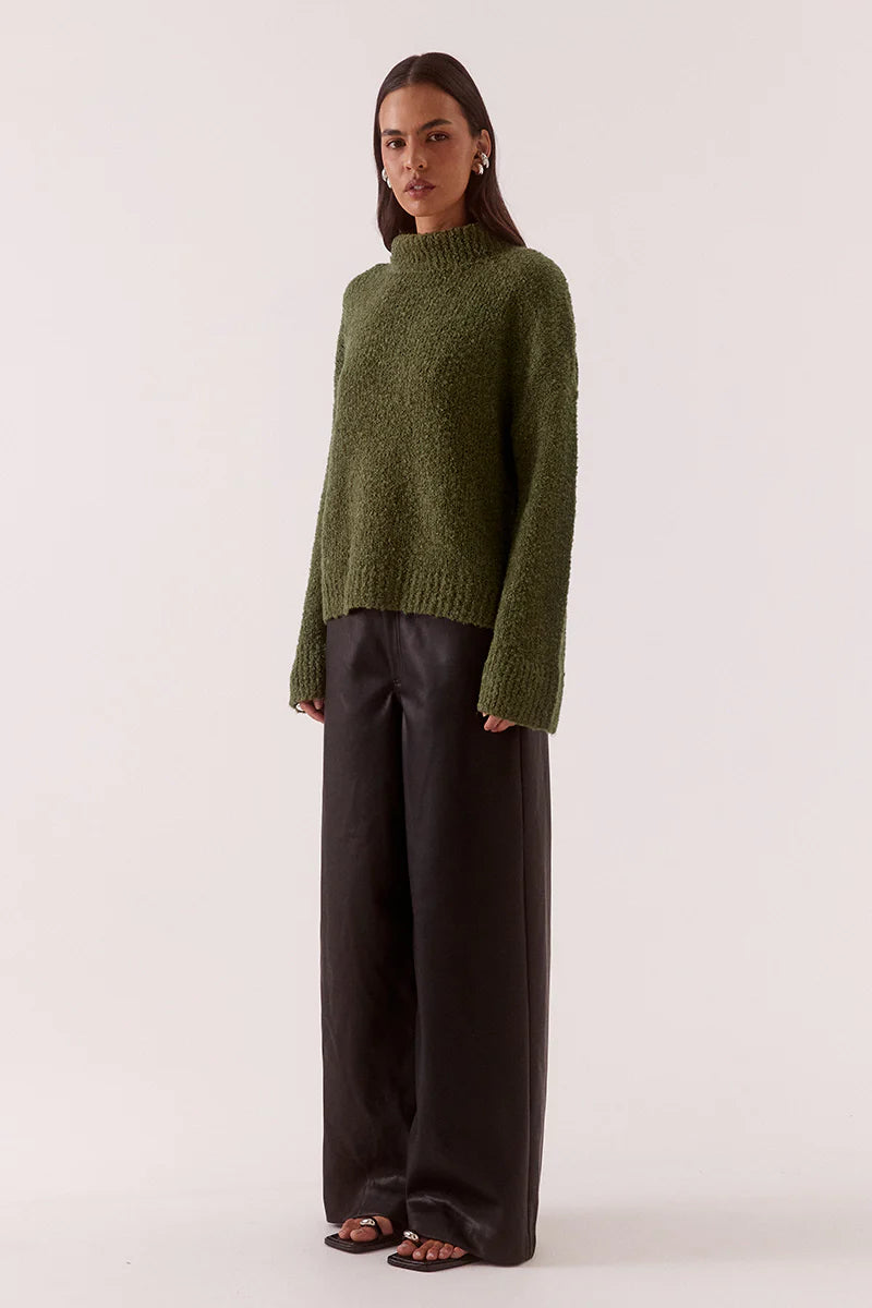Woman wearing a green sweater and black pants on a white background
