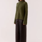 Woman wearing a green sweater and black pants on a white background